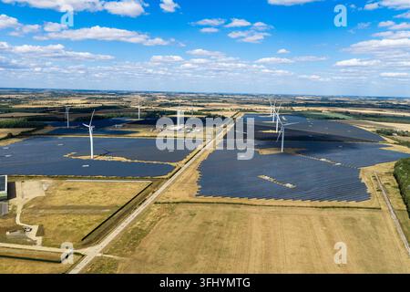 Renewable energy site showing many black solar panels and tall white wind turbines located in a rural landscape under a clear blue sky on a bright sun Stock Photo