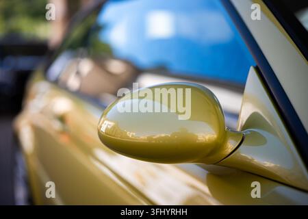 Close up shot of a sleek yellow sports coupe car side mirror with a smooth paint reflection and shallow depth of field parked outdoors in daylight. Stock Photo