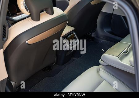 View into the rear seating area of a modern luxury car showing light beige leather seats, generous legroom, floor carpet, and rear climate control uni Stock Photo