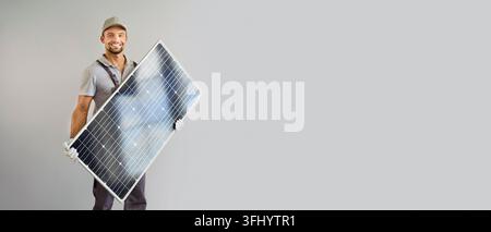 Smiling Solar Technician Holding Photovoltaic Panel Against Gray Background Stock Photo