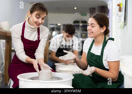 Two young women sculpting ceramic product on potter's wheel in workshop Stock Photo