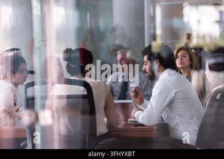 A diverse team of professionals seated around a glass boardroom table, focused on discussion and strategy planning. Colleagues take notes, share ideas Stock Photo