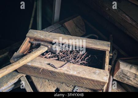 Tammela, Finland - 25.07.2026: Vintage hammer resting on a wooden crate filled with oxidized iron nails in a dark shed Stock Photo