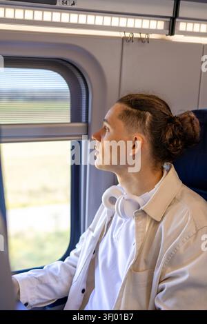 Thoughtful mid adult traveler looking out of train window while working on laptop. Business trip optimization remote employee corporate worker analyzi Stock Photo