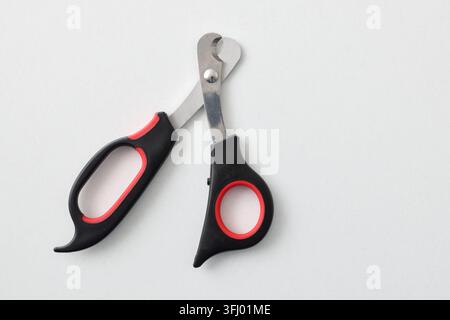 A pair of pet nail trimming scissors with black and red handles lies on a white background. The image highlights the tool’s design, material, and groo Stock Photo