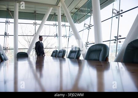 Business executive standing in modern glass boardroom overlooking city during a meeting Stock Photo