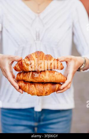 Woman in white shirt holds stack of fresh croissants Stock Photo