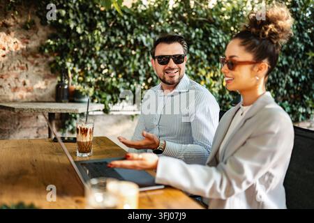 Business colleagues collaborating working on laptop at outdoor cafe Stock Photo