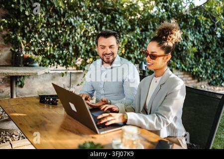 Two business professionals collaborating and discussing work using a laptop in an outdoor setting Stock Photo
