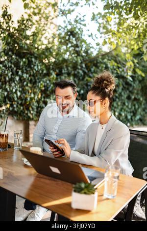 Couple sitting outdoors at cafe using laptop and smart phone Stock Photo