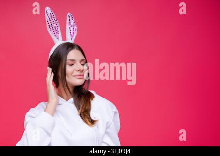 Peaceful Caucasian Woman with Pink Bunny Ears on Red Background Easter Mood Portrait Stock Photo