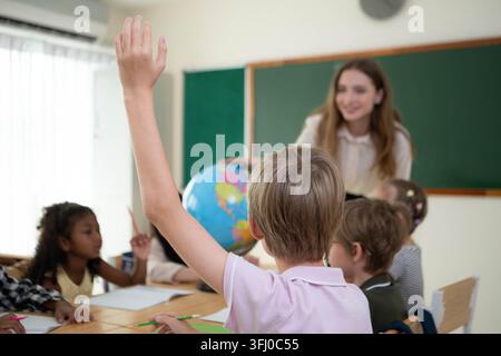 The teacher is providing guidance to children in a multiethnic classroom during a creative activity in the elementary school Stock Photo