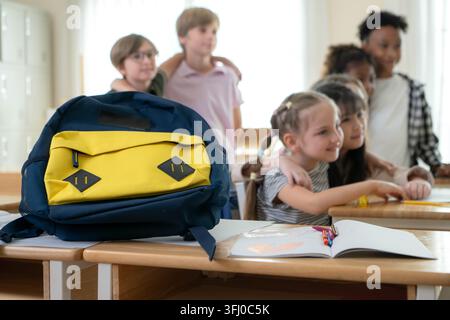 Group of happy elementary students raising hands together in a bright classroom with their school bags in the foreground Stock Photo