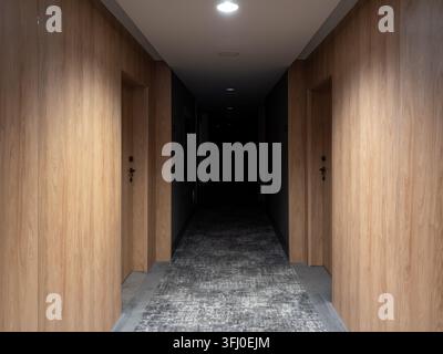 The perspective view along a narrow corridor featuring sleek wooden accents and recessed lighting, creating a somber ambiance suitable for architectur Stock Photo