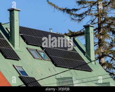 Black photovoltaic modules mounted onto a corrugated green rooftop of a residential building, capturing sunlight to support clean electrical power gen Stock Photo