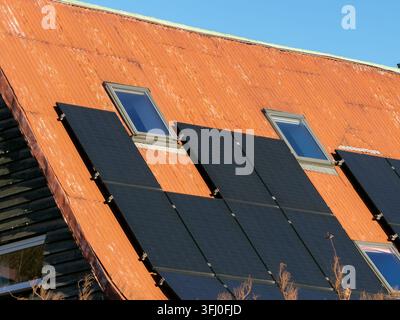Black photovoltaic modules mounted on a rustic corrugated red roof with skylights, reflecting an eco-friendly transition to sustainable power sources Stock Photo