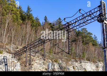 Metal catenary structures support electrical cables above a railway track near a rocky slope, symbolizing engineering precision and connectivity in pu Stock Photo