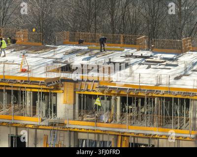 Laborers working on the concrete framework of a multistory project using safety equipment and steel reinforcements, representing industrial growth and Stock Photo