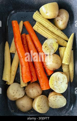 Seasoned baby potatoes, carrots and baby sweetcorn prepared in a roasting tray for cooking Stock Photo