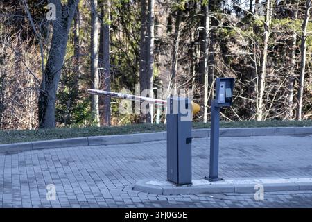 A metal security barrier arm blocks entry to a restricted area on a concrete block road, where modern intercom technology facilitates visitor communic Stock Photo