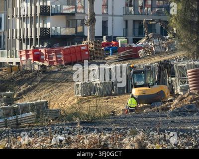 Szklarska Poreba, Poland - December 18, 2025: An operator stands beside an excavator on a muddy site filled with construction materials like pallets a Stock Photo