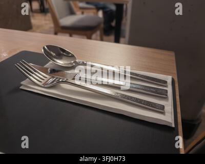 Shiny stainless steel cutlery arranged neatly on a folded paper napkin upon a textured tabletop, creating an inviting dining atmosphere for gourmet me Stock Photo