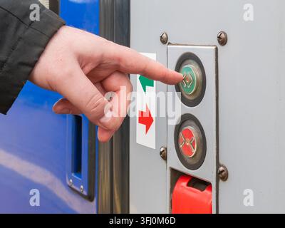 Close-up of a finger pushing an illuminated button on a train door frame, signaling the start of a commute and the ease of access in urban rail infras Stock Photo