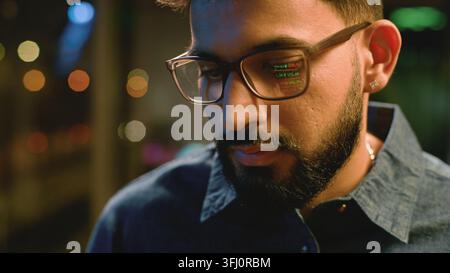Indian business man using digital tablet device at night office lights reflection graph data reflect in glasses. Concentrated Arabian businessman male Stock Photo