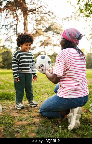 Mother and child playing soccer ball in park Stock Photo