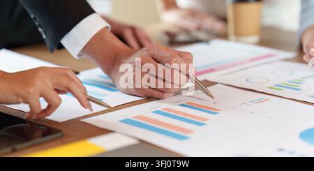 A diverse business team collaborates in a meeting, pointing at financial data and charts on paper. This image represents strategic planning and teamwo Stock Photo
