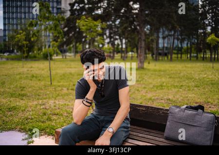Young man making phone call on park bench smiling Stock Photo