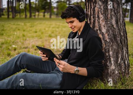 Young man using tablet and headphones outdoors in park Stock Photo