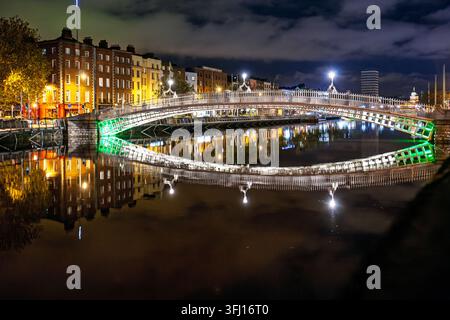 Night view of the iconic Ha'penny Bridge (Half Penny Bridge) spanning the River Liffey in Dublin, Ireland. City lights and bridge illumination create Stock Photo