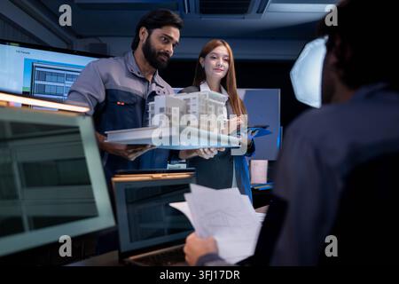 Engineering and business professionals discussing architectural building model and project development strategy in modern collaborative workspace Stock Photo