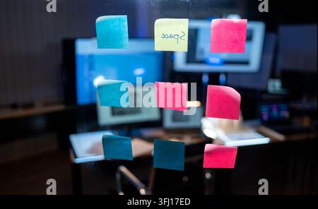 Colorful sticky notes attached to glass board in creative office workspace for project planning and brainstorming session Stock Photo