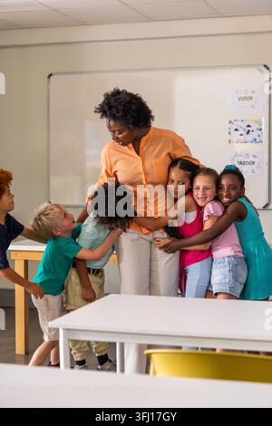 African American teacher in orange top hugging kids and smiling at school whiteboard VISION poster. Classroom, children, stock, colorful, warmth, educ Stock Photo