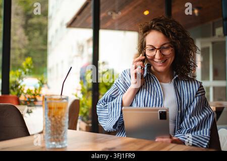 Woman talking on smartphone using digital tablet in cafe Stock Photo