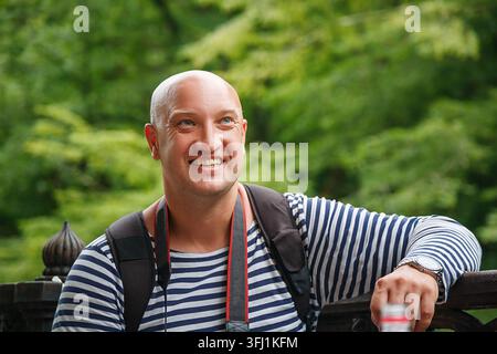 Smiling Bald Man with Backpack in Striped Shirt at Green Park Stock Photo