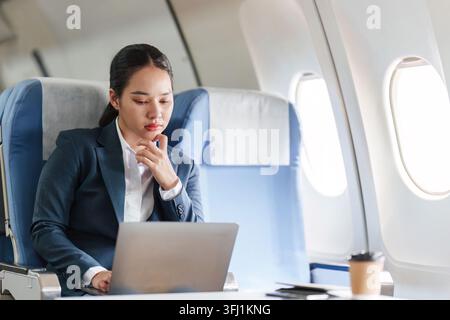 Asian businesswoman working on laptop during airplane flight Stock Photo