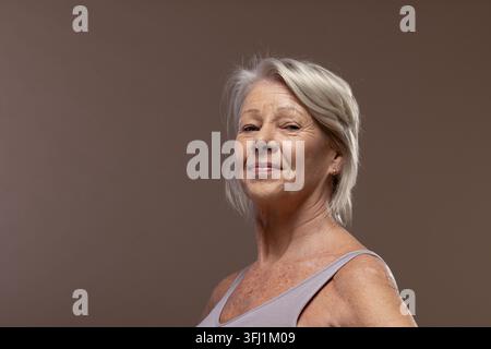 Senior female posing in studio backdrop, wearing mauve tank and stud earring, getting studio light Stock Photo