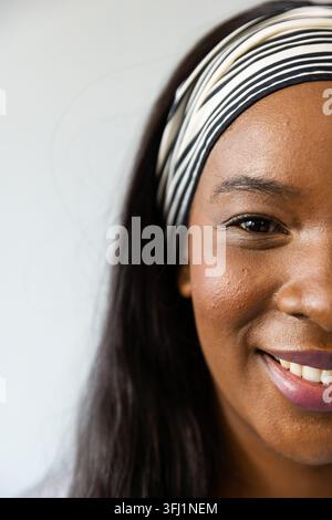 African woman smiling, showing mauve lips with striped headband against pale wall, copy space Stock Photo
