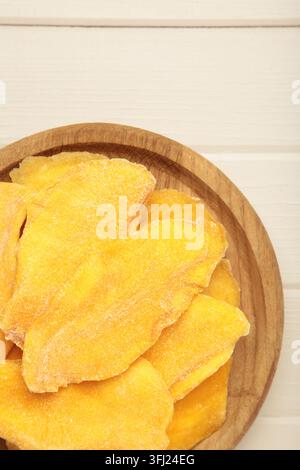 Slices of dried mango on wooden plate on light wooden background. Top view Stock Photo