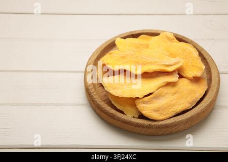 Slices of dried mango on wooden plate on light wooden background. Top view Stock Photo