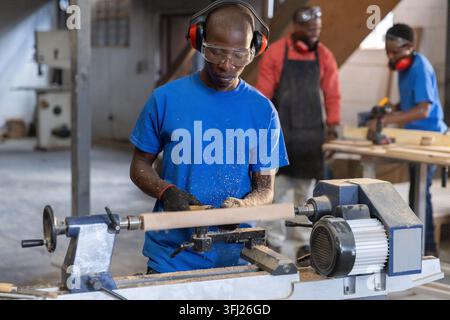 African American male coworkers operating wood lathe and using power drill on workbench in workshop. Craftsmanship, woodworking, Stock Photo