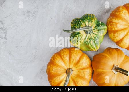Green and orange pumpkins arranged in corner position on smooth marble background representing autumn harvest variety for seasonal grocery or culinary Stock Photo
