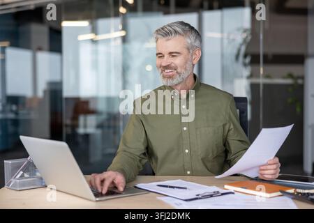 Businessman working on laptop and reviewing documents at office desk, professional man analyzing financial reports and corporate data for business growth and success in a modern corporate environment. Stock Photo