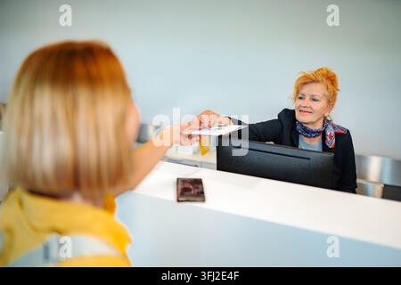 Employee at reception desk assisting customer with checking in and passing documents Stock Photo