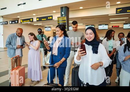 Diverse group of people using smartphones in airport Stock Photo