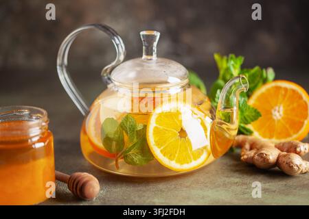 Glass teapot with hot citrus tea from oranges, lemons, apples, ginger and mint. Healthy drink on dark background Stock Photo