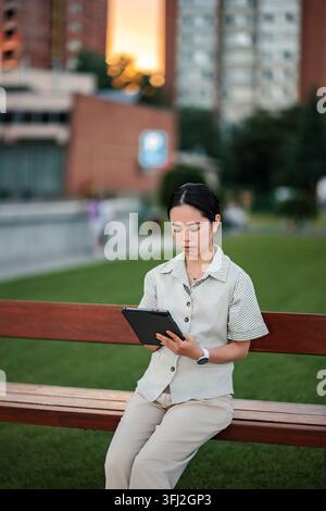 Asian woman working remotely on tablet in city park Stock Photo